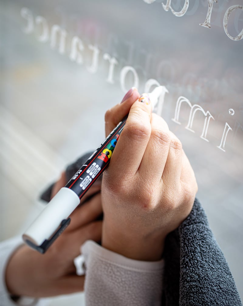 Pauline Seither peint sur une vitrine à l'aide d'un stylo acrylique